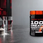 Original Scitec creatine monohydrate tub beside gym equipment and a glass of water